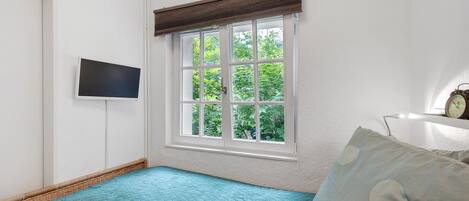 Quarto com uma janela grande, televisão de tela plana, relógio e cama com colcha azul.