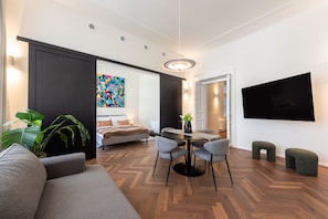 A modern living room with a sofa, a dining table with chairs, a bed, and a TV mounted on the wall. - High-End 2BR Apt. with A/C & Parking by EasyBNB Premium (Prague)