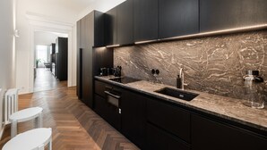 Une cuisine moderne avec des meubles de couleur sombre, un pare-feu en marbre et un plancher en bois disposé en motif chevron.