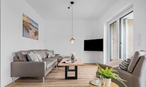 A modern living room with a sofa, coffee table, and a TV mounted on the wall. - Vacation apartment Waterkant Büsum directly on the beach with sea view over the harbor (Büsum)