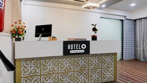 Ein Empfangstresen mit einem 'HOTELO'-Schild, einem Flachbildfernseher, einer Vase mit Blumen und einer Topfpflanze.