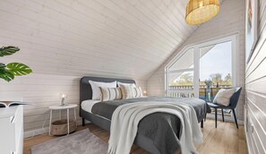 Ein Schlafzimmer mit Bett, Nachttisch, Lampe und Blick durch ein großes Fenster.