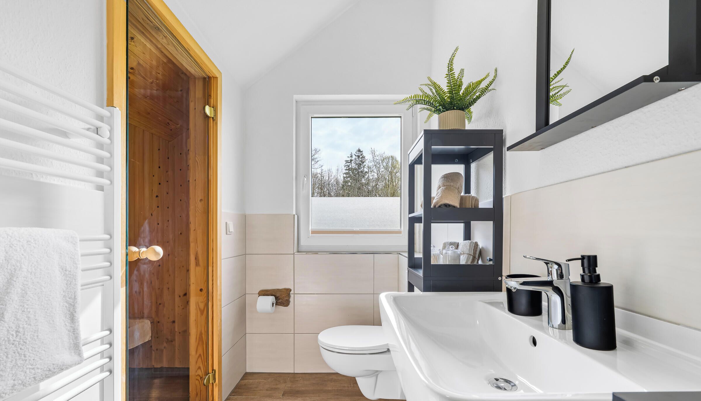 Een badkamer met een wit wastafel, toilet, houten deur, raam en een plank met handdoeken.