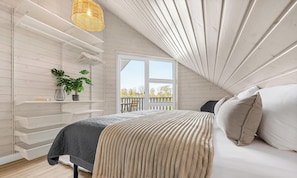 A bedroom with a bed, a hanging light fixture, a window, and a plant.