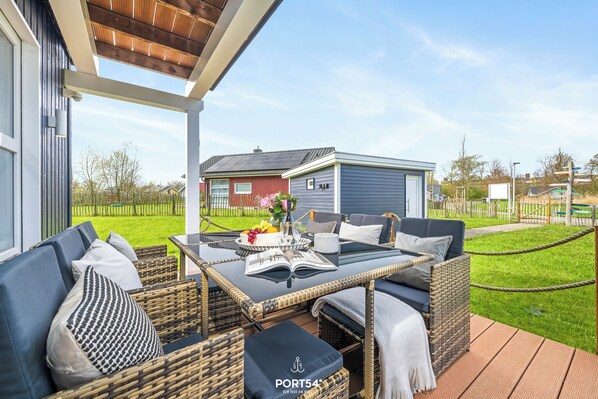 Eine Terrasse im Freien mit Korbmöbeln, einem Glastisch und einem Buch.
