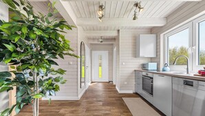 Une cuisine moderne avec un plancher en bois, des meubles blancs, une grande fenêtre et une plante en pot.