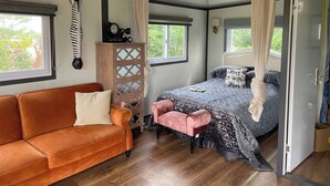 Un dormitorio con cama, sofá, aparador de madera y ventana.