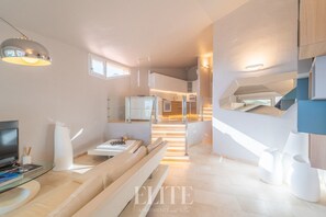 Ein modernes Wohnzimmer mit einer Couch, einem Couchtisch und einem Fernseher. Eine Treppe führt zu einer oberen Ebene.