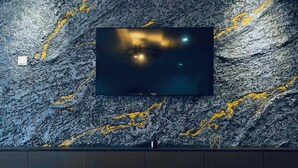 Una sala de estar moderna con un televisor de pantalla plana grande montado en una pared texturizada, dos mesas redondas con patas de metal y una alfombra mullida.