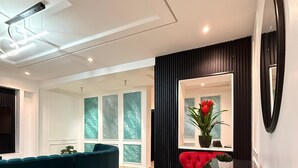 Una sala de estar moderna con un sofá azul verdoso curvo, una silla roja, una consola blanca y un espejo grande.