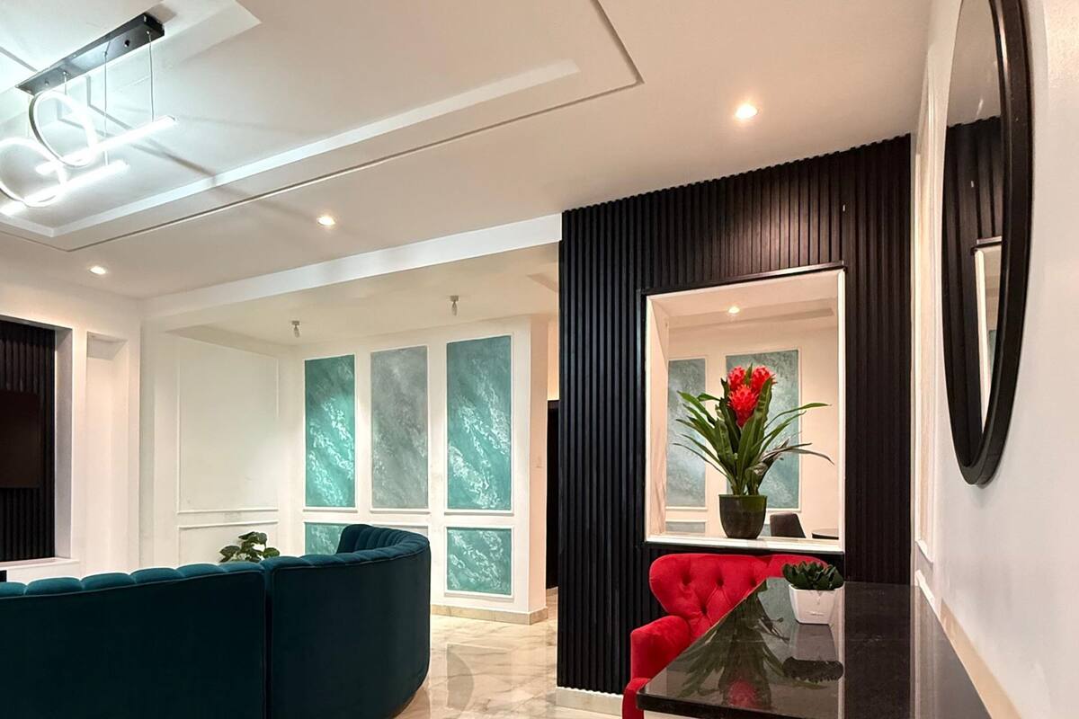 Un salon moderne avec un canapé incurvé de couleur turquoise, un fauteuil rouge, une console blanche et un grand miroir.