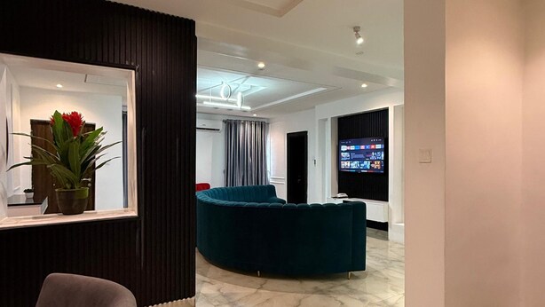 Un moderno vestíbulo de hotel con una zona de estar curva, un televisor de pantalla plana grande y una planta en maceta.