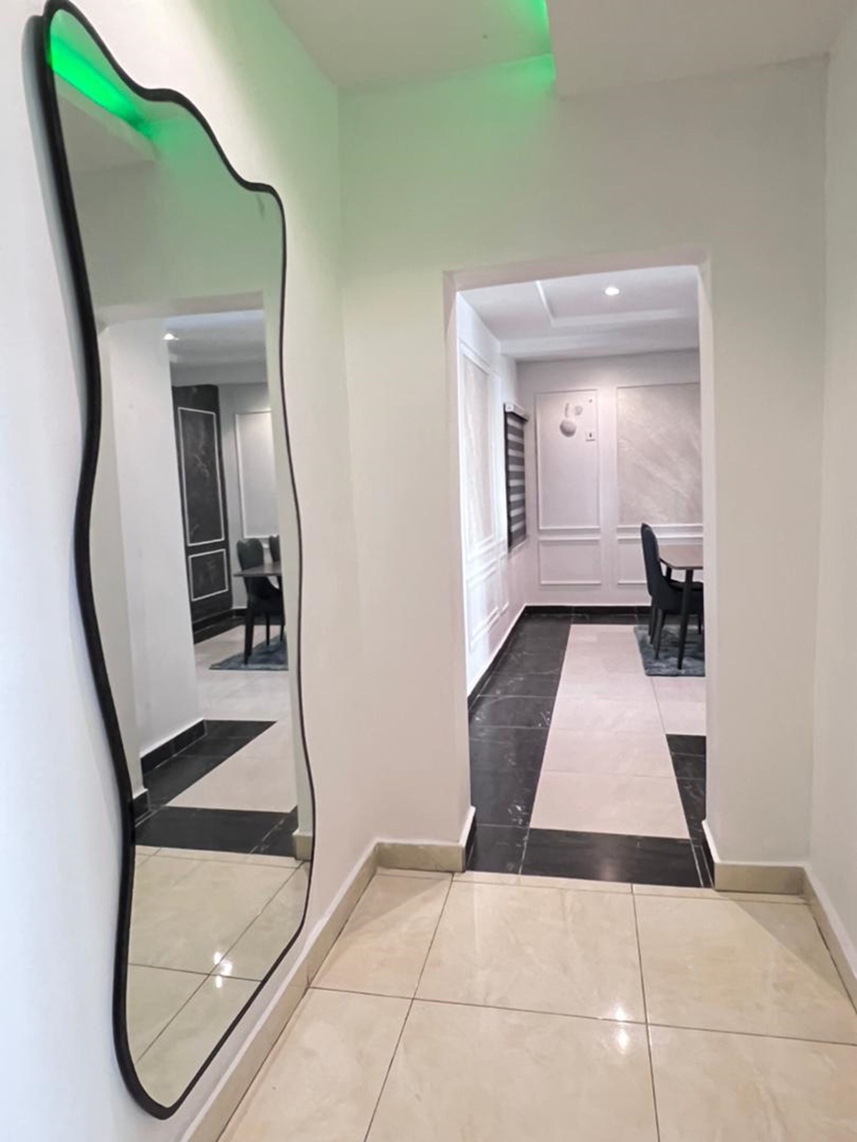 A hallway with a large mirror, a dining area with a table and chairs, and a door leading to another room.