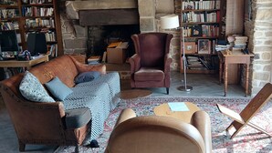 Ein gemütliches Wohnzimmer mit Kamin, Ledermöbeln und Bücherregalen voller Bücher.