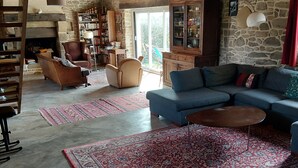Ein geräumiges Wohnzimmer mit Kamin aus Stein, einem blauen Sofa und einem großen Teppich.