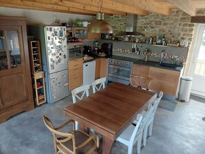 A kitchen with wooden cabinets, a refrigerator, a stove, and a dining table with chairs. - Longère (traditional long house) near the Golfe du Morbihan (Saint-Avé)