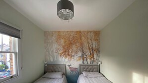 A room with two beds, a chandelier, a mural of trees, and a window. - Delightful 2 Bedroom House Central Windsor. Walk to Castle, River! (Windsor)