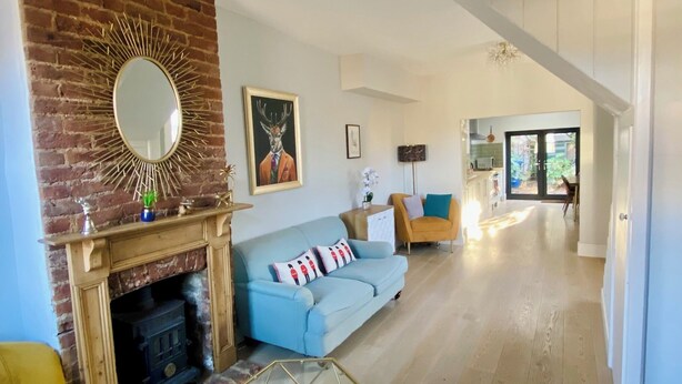 A living room with a fireplace, a blue sofa, a yellow armchair, and a dining area in the background. - Delightful 2 Bedroom House Central Windsor. Walk to Castle, River! (Windsor)