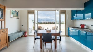 Een moderne keuken met blauwe kastjes, een eettafel met stoelen en uitzicht door de open deur.
