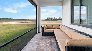 A covered outdoor seating area with a view of a grassy field and trees. - Nick House (Lehigh Acres)