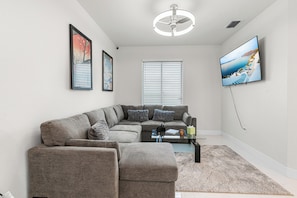 A modern living room with a sectional sofa, a flat-screen TV, and a ceiling fan.