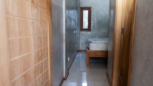 A narrow hallway with a wooden door on the left, a small window on the right, and a wooden bench in the center. - Monkey Palms (Gili Air)