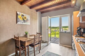 A dining area with a wooden table and chairs, a painting of sunflowers, and a view through a glass door to an outdoor deck. - Apartment "Haus Schönblick" with Spacious Balcony in the Bavarian Odenwald (Amorbach)
