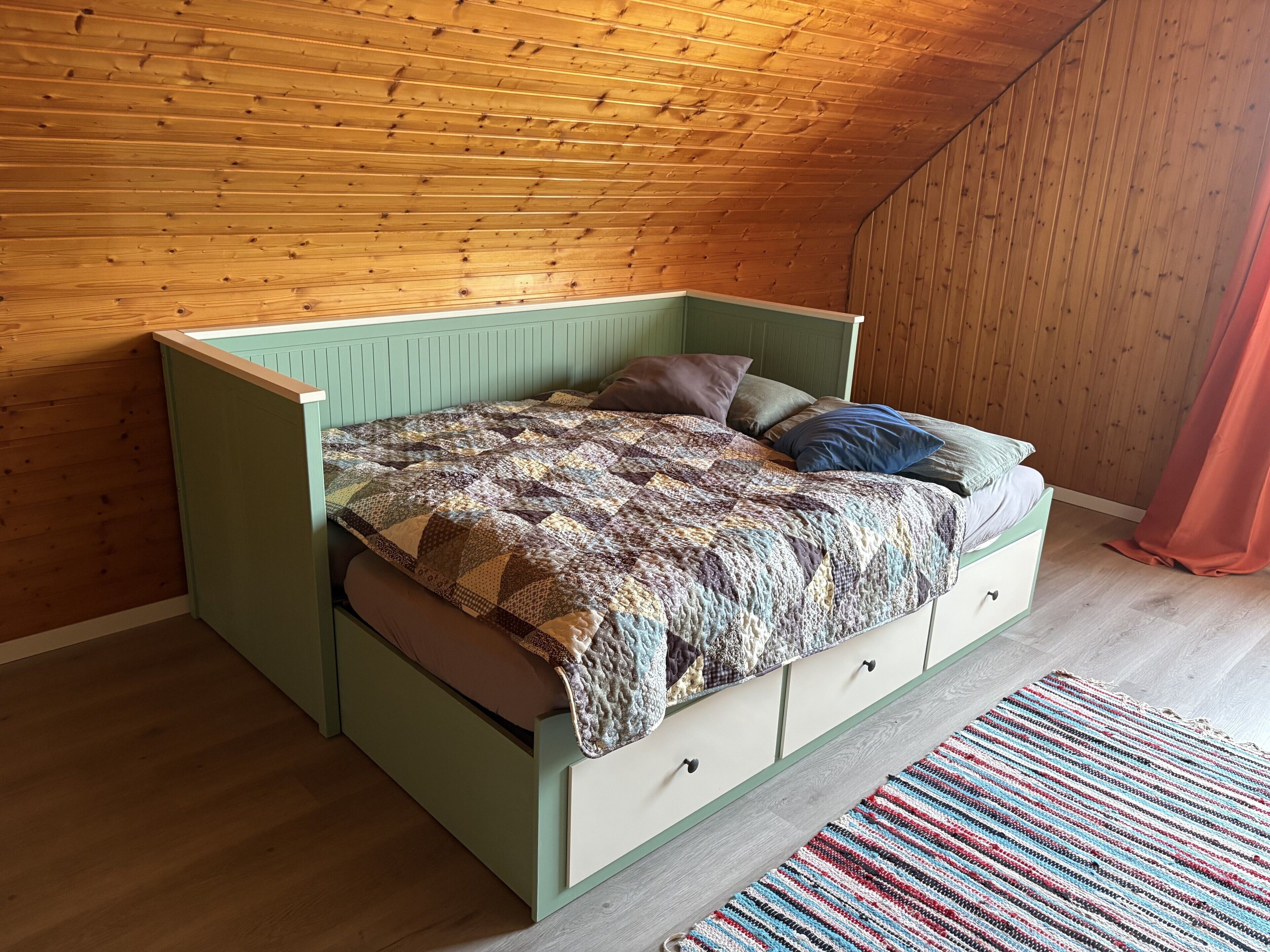 Un lit simple avec une couette, un plafond en bois à pente et un mur vert.