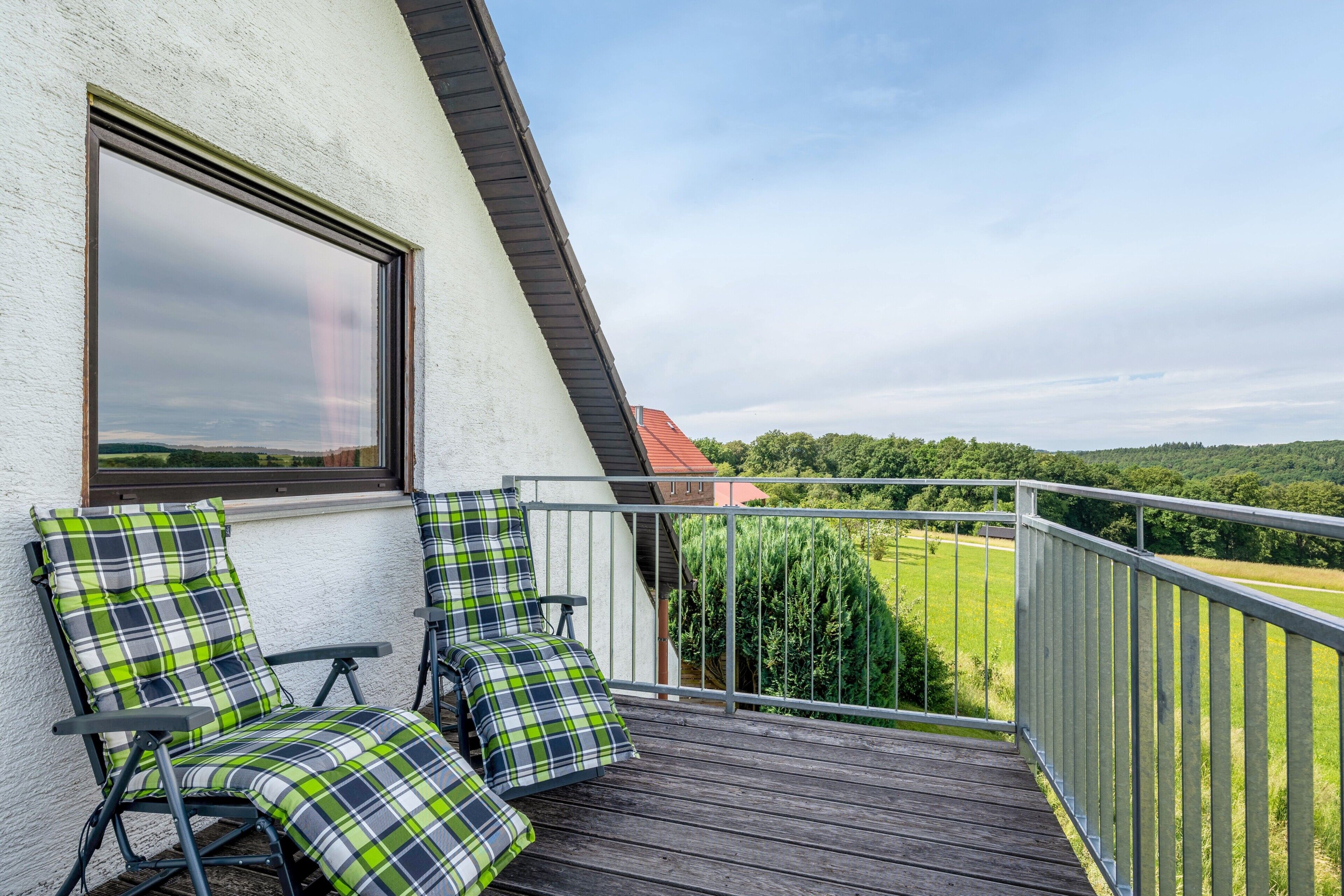Un balcon avec deux chaises et une grande fenêtre donnant sur un paysage verdoyant.