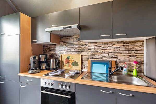 A compact kitchen with a stone backsplash, a coffee maker, a toaster, and a sink.
