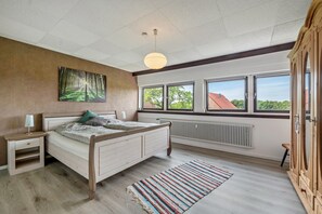 A bedroom with a bed, nightstand, dresser, radiator, windows, and a view of the outside. - Apartment "Haus Schönblick" with Spacious Balcony in the Bavarian Odenwald (Amorbach)