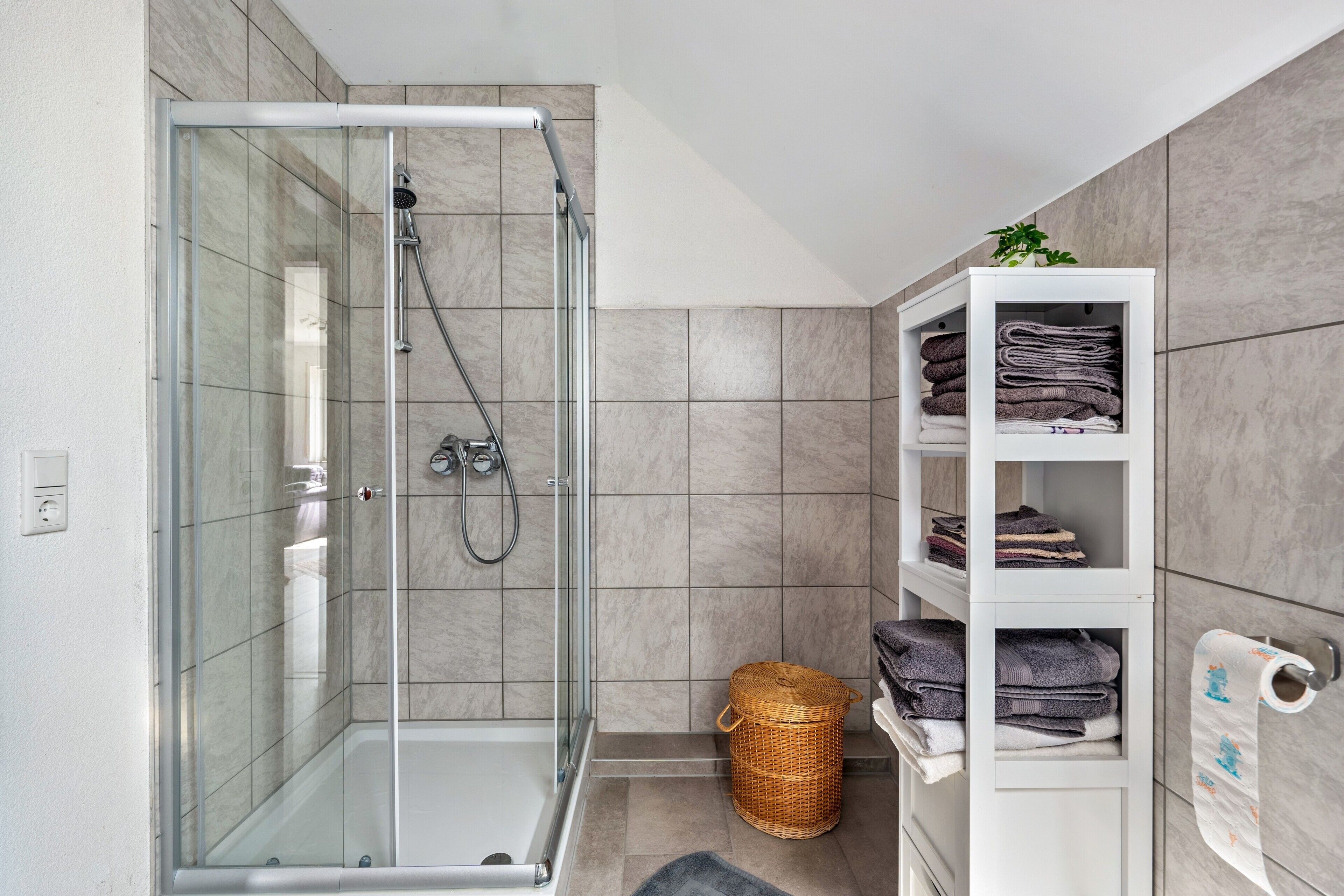 Une salle de bain moderne avec une douche à parois de verre, un porte-serviettes blanc et un panier en osier.