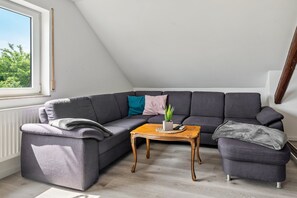 A corner living room with a grey sectional sofa, a wooden coffee table, and a small potted plant. - Apartment "Haus Schönblick" with Spacious Balcony in the Bavarian Odenwald (Amorbach)