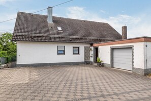 A single-story house with a tiled roof, a garage, and a paved driveway. - Apartment "Haus Schönblick" with Spacious Balcony in the Bavarian Odenwald (Amorbach)