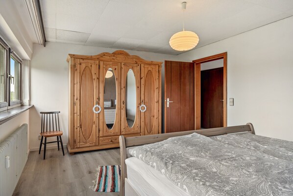 Un dormitorio con cama, armario de madera y una silla.