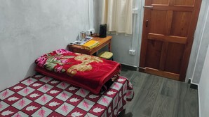 A small, neatly arranged bedroom with a bed, a wooden nightstand, a small table, and a door.