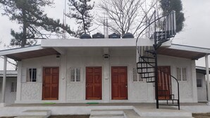 A two-story building with a white exterior, three wooden doors, a spiral staircase, and a small outdoor area with steps.
