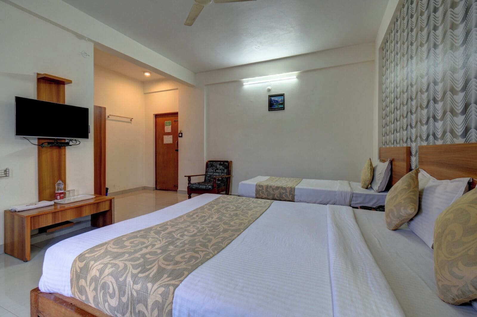 A hotel room with two beds, a TV, a chair, and a desk.