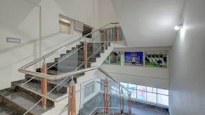 A multi-level interior with a glass and metal staircase, a window with a view, and a wall with framed pictures. - ATITHI COMFORTS (Somvarpet)