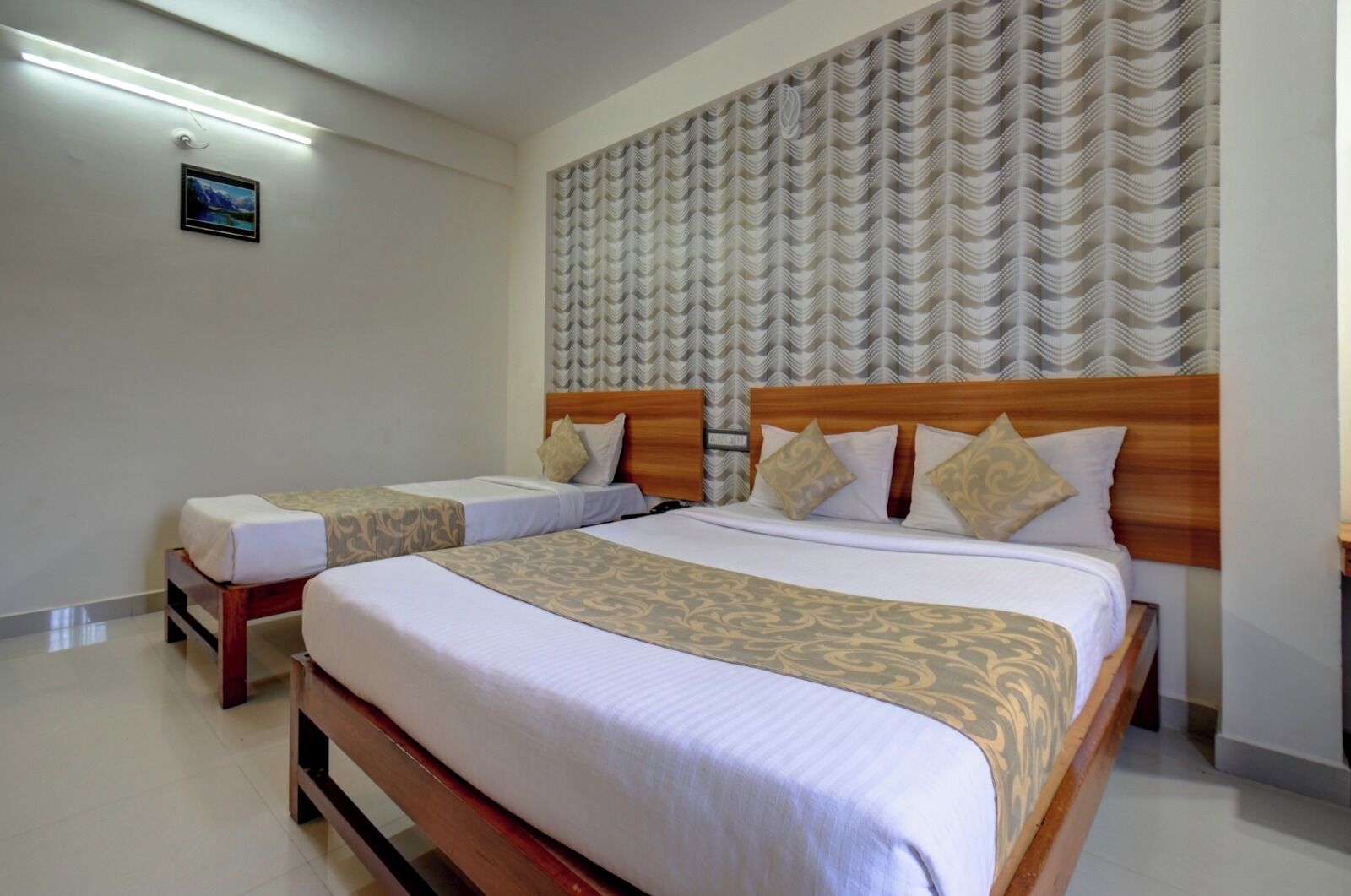 Two single beds with wooden frames and headboards, a patterned wall headboard, a flat-screen TV mounted on the wall, and a tiled floor.