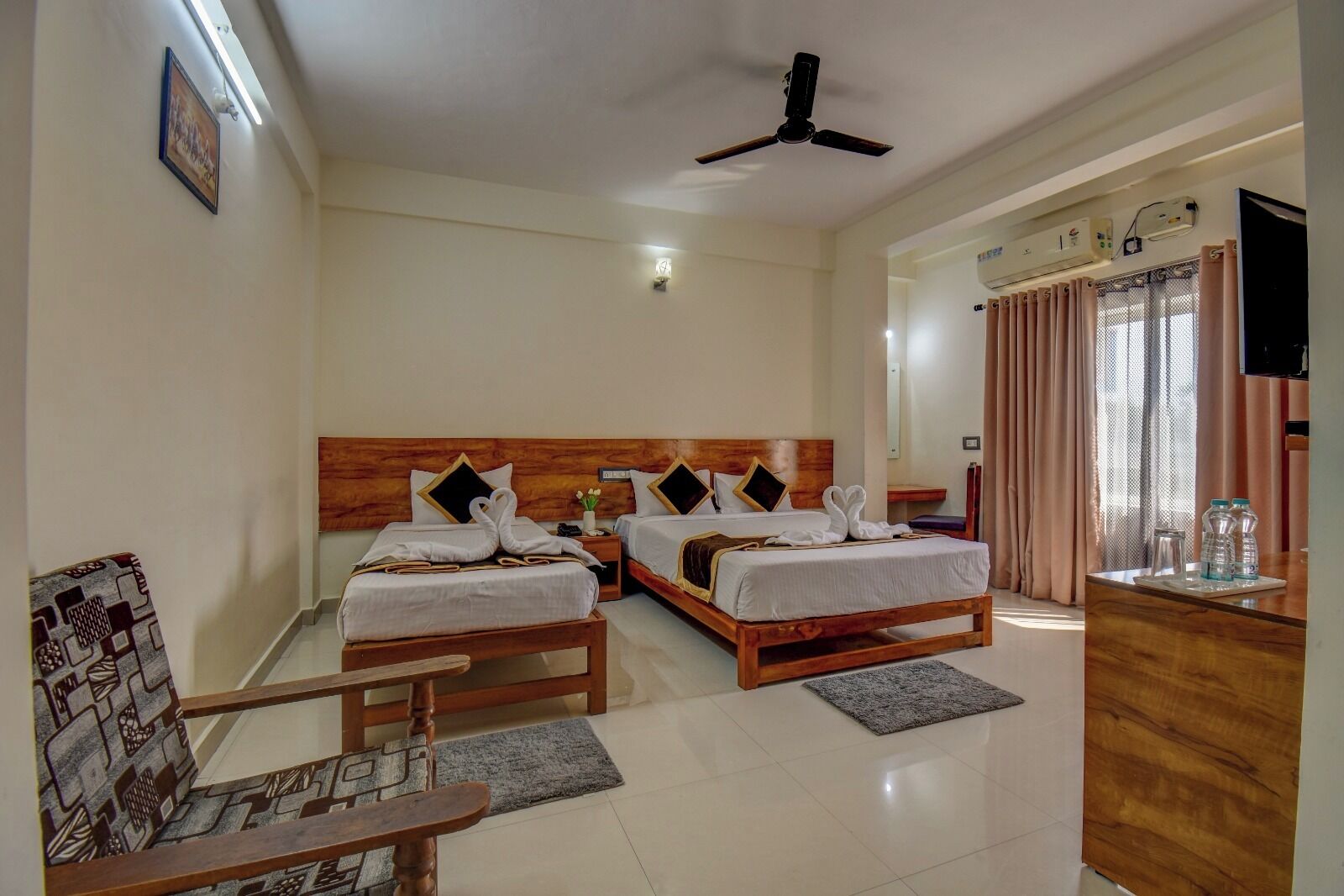 A hotel room with two wooden beds, a ceiling fan, a TV, and a desk with a mirror.