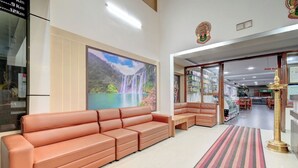 A hotel lobby with a large sofa, a mural of a waterfall, a reception desk, and a carpeted area. - ATITHI COMFORTS (Somvarpet)