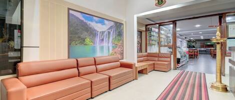 A hotel lobby with a large sofa, a mural of a waterfall, a reception desk, and a carpeted area.