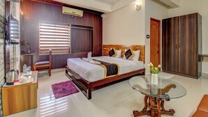 A modern hotel room with a large bed, a glass coffee table, a wardrobe, and a desk with a kettle. - ATITHI COMFORTS (Somvarpet)