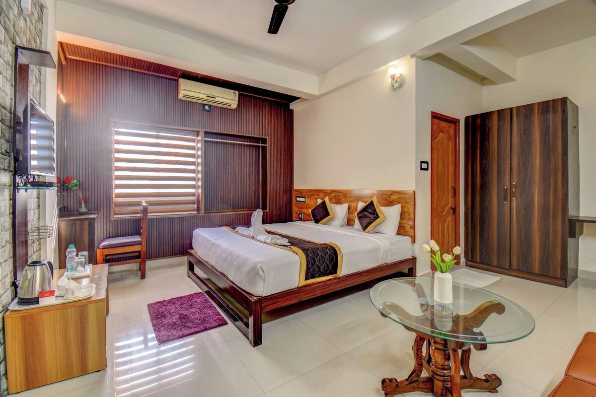 A modern hotel room with a large bed, a glass coffee table, a wardrobe, and a desk with a kettle.