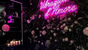 Ein Zimmer mit einem Neonlichtschild mit der Aufschrift 'Vibrazioni d'Amore' und einer Blütenwand.