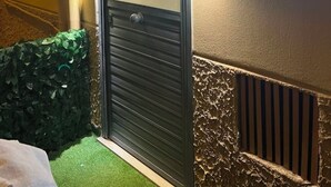 Eine Tür mit einer Metallklinke, einem an der Wand befestigten Schild, einem Lüftungsgitter und einer kleinen Zimmerpflanze.