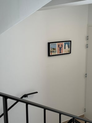 Eine Treppe mit Handlauf, eine weiße Wand und ein gerahmtes Bild mit Illustrationen.