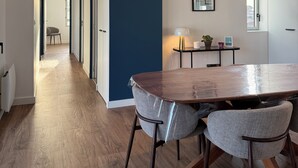 A modern interior with a wooden dining table, two chairs, a blue accent wall, and a hallway leading to another room. - Apartment with terrace – Close to the sea and Royan city center (Royan)