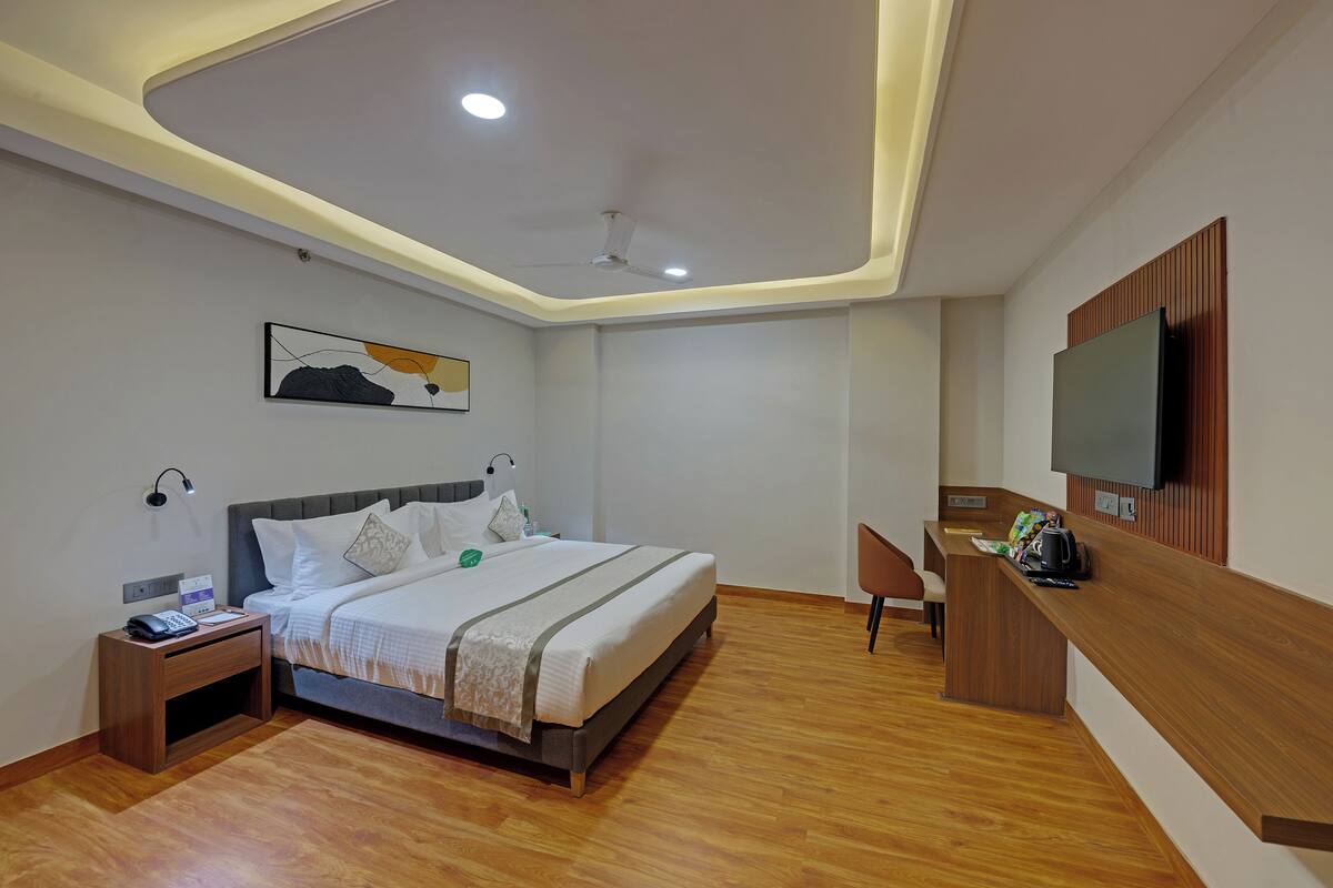 A hotel room with a bed, bedside table, lamp, desk, chair, and TV.